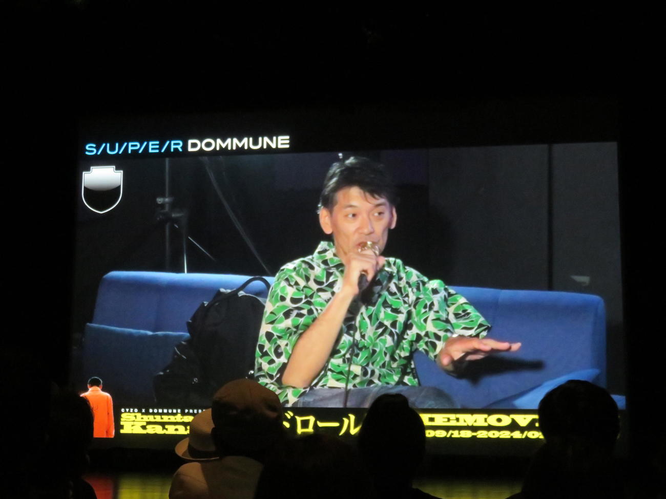 会場で一部公開された映画「エンドロール　THE MOVIE」に出演する叶井俊太郎さん（左）と宇川直宏氏。真ん中はリモート出演の中原昌也氏のイラスト