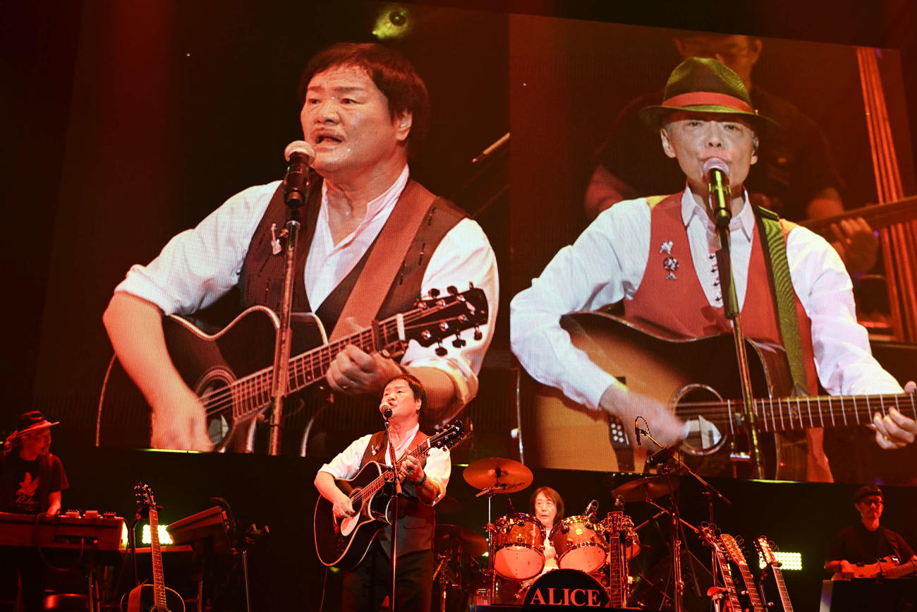 「アリス　コンサート2024 ALICE FOREVER～アリガトウ～」でパフォーマンスするアリス。中央左から堀内孝雄、矢沢透。後ろの映像は堀内孝雄（左）と谷村新司さん（写真・中嶌英雄）
