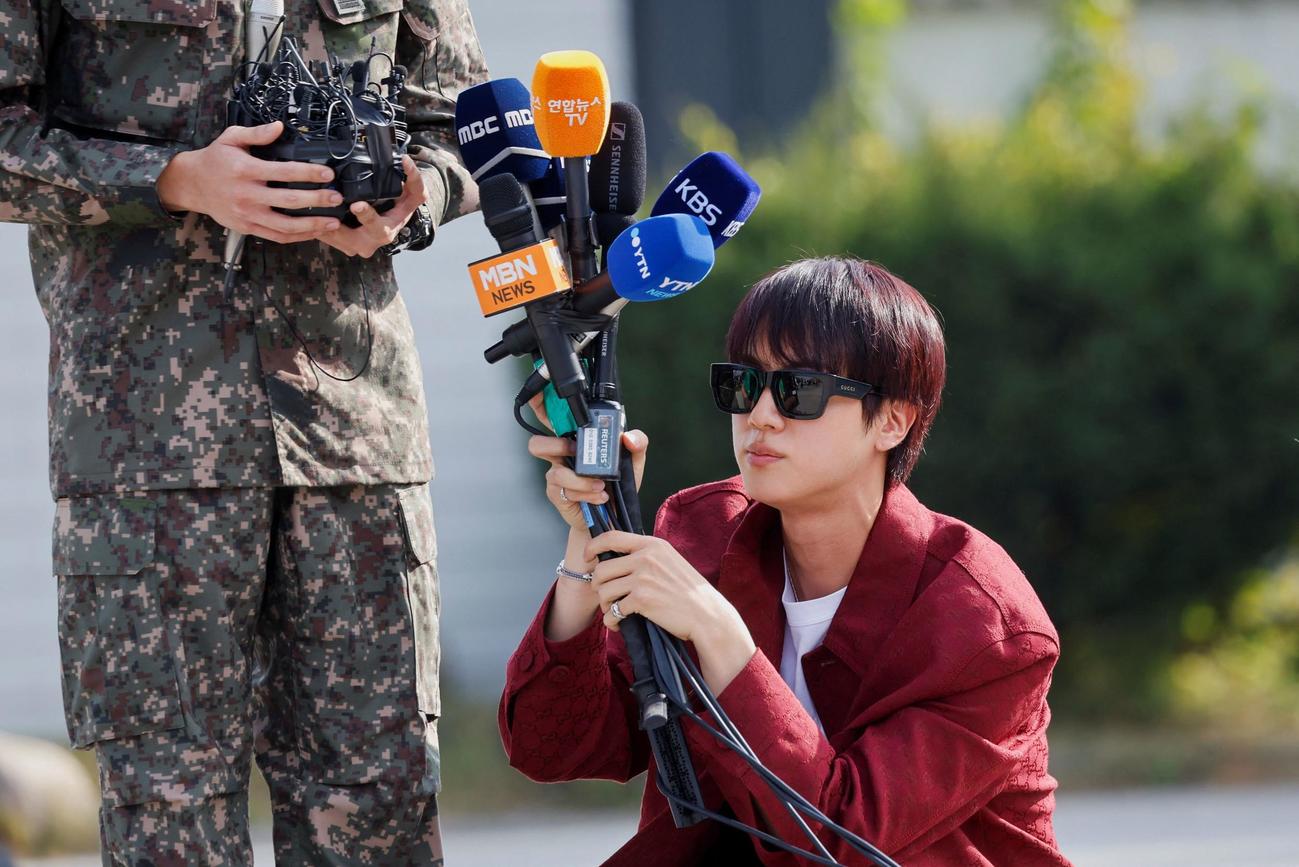 取材に応えるBTSのJ－HOPE（左）の下でマイクを持つJIN（ロイター）