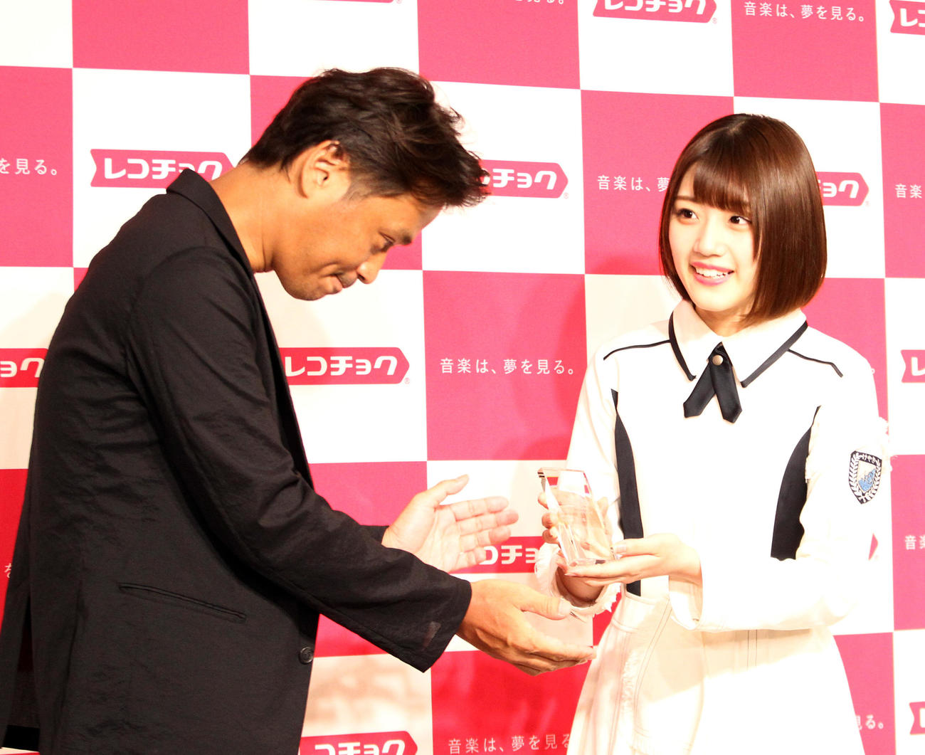 レコチョク上半期ランキング2018の新人アーティストランキングで1位を獲得したけやき坂46（ひらがなけやき）の佐々木美玲（右）は、レコチョク執行役員柴崎栄太郎氏からトロフィーを受け取る（2018年7月撮影）