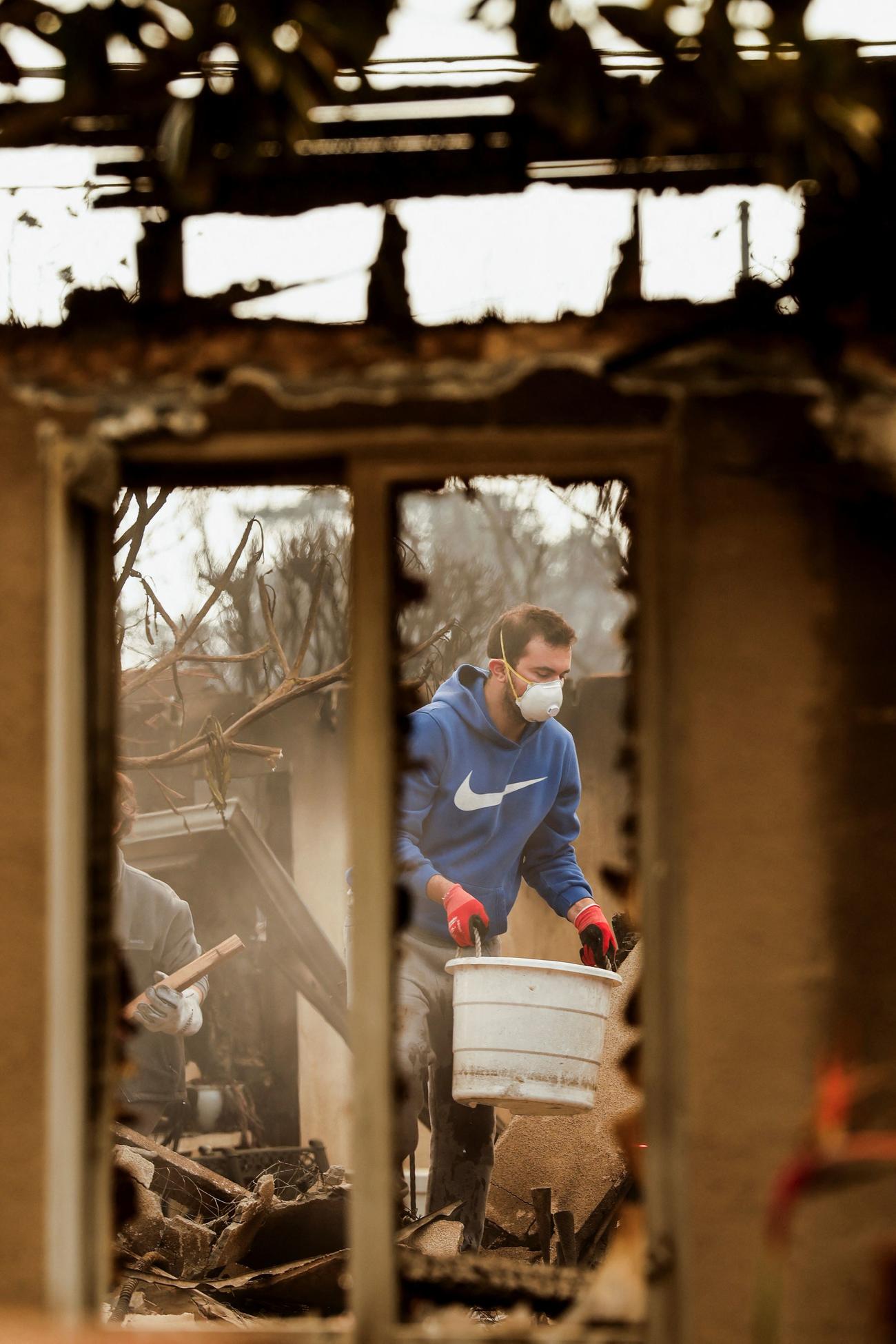 カリフォルニア州アルタデナで、火災によって焼失した家屋を住民たちが掘り起こす中、バケツで水を運ぶ男性（２０２５年１月９日、ロイター）