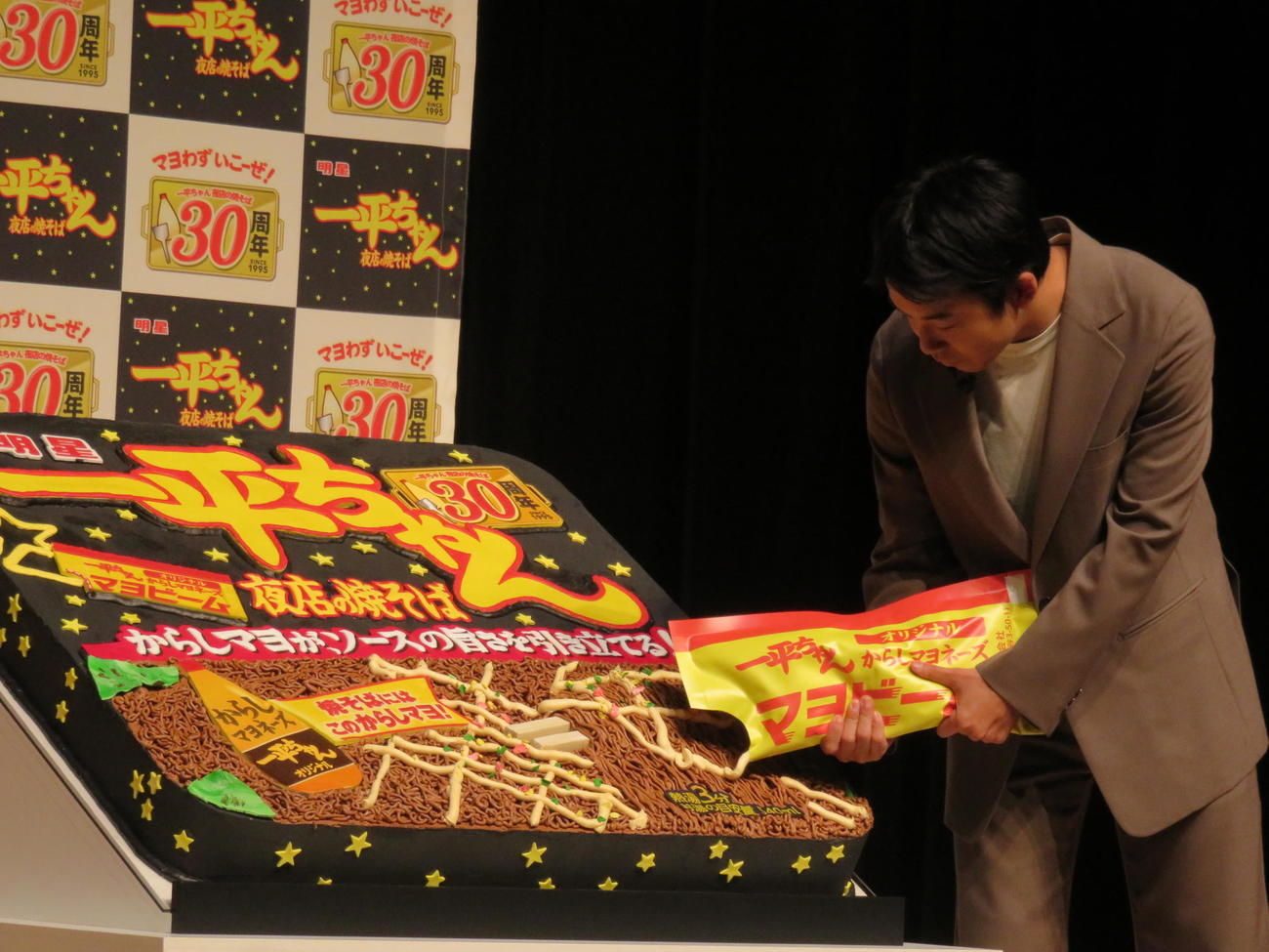 「明星　一平ちゃん夜店の焼そば」発売30周年記念発表会で、巨大ケーキにマヨビームで生クリームをかける仲野太賀