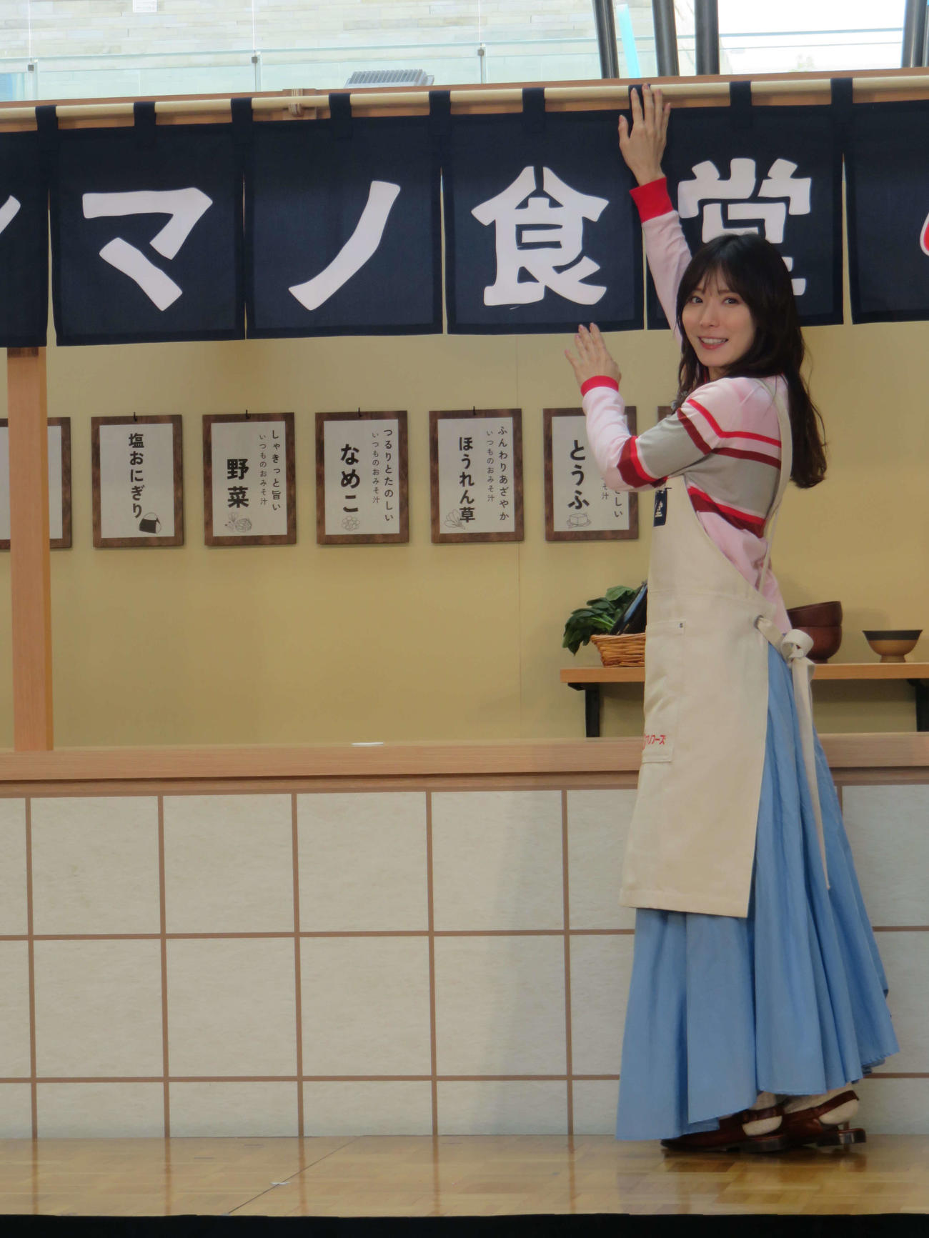 エプロン姿で「アマノ食堂」ののれんを掛ける松岡茉優