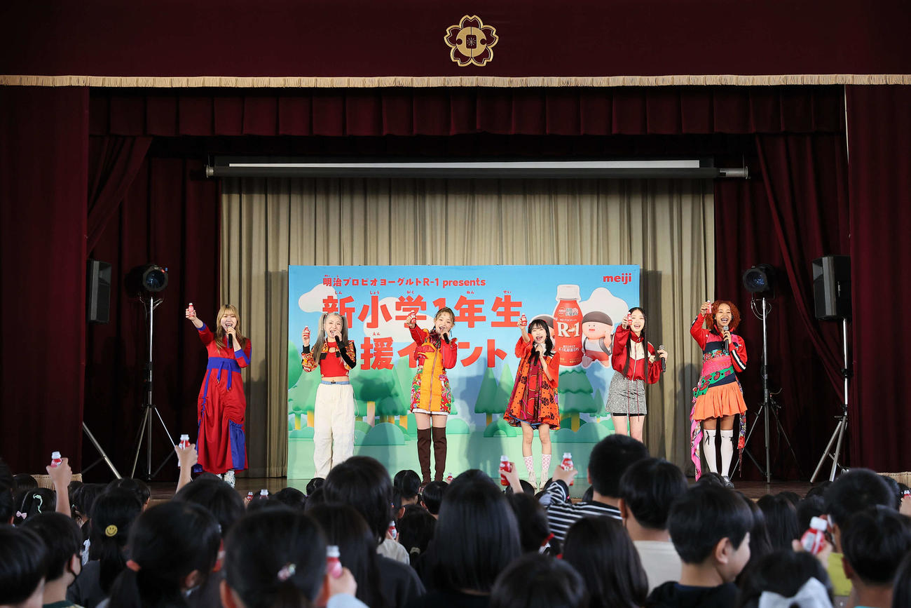 「明治プロビオヨーグルトR－1 presents　新小学1年生応援イベント」に登場し、小学生と乾杯するLittle Glee Monster。左からかれん、MAYU、ミカ、アサヒ、結海、miyou