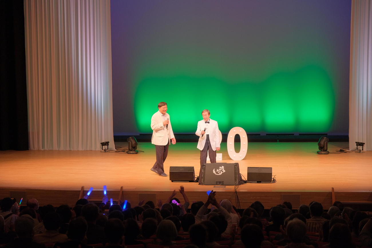 「一過性脳虚血発作」と診断されて入院し、復帰したステージで歌唱する橋幸夫（右）と石田社長