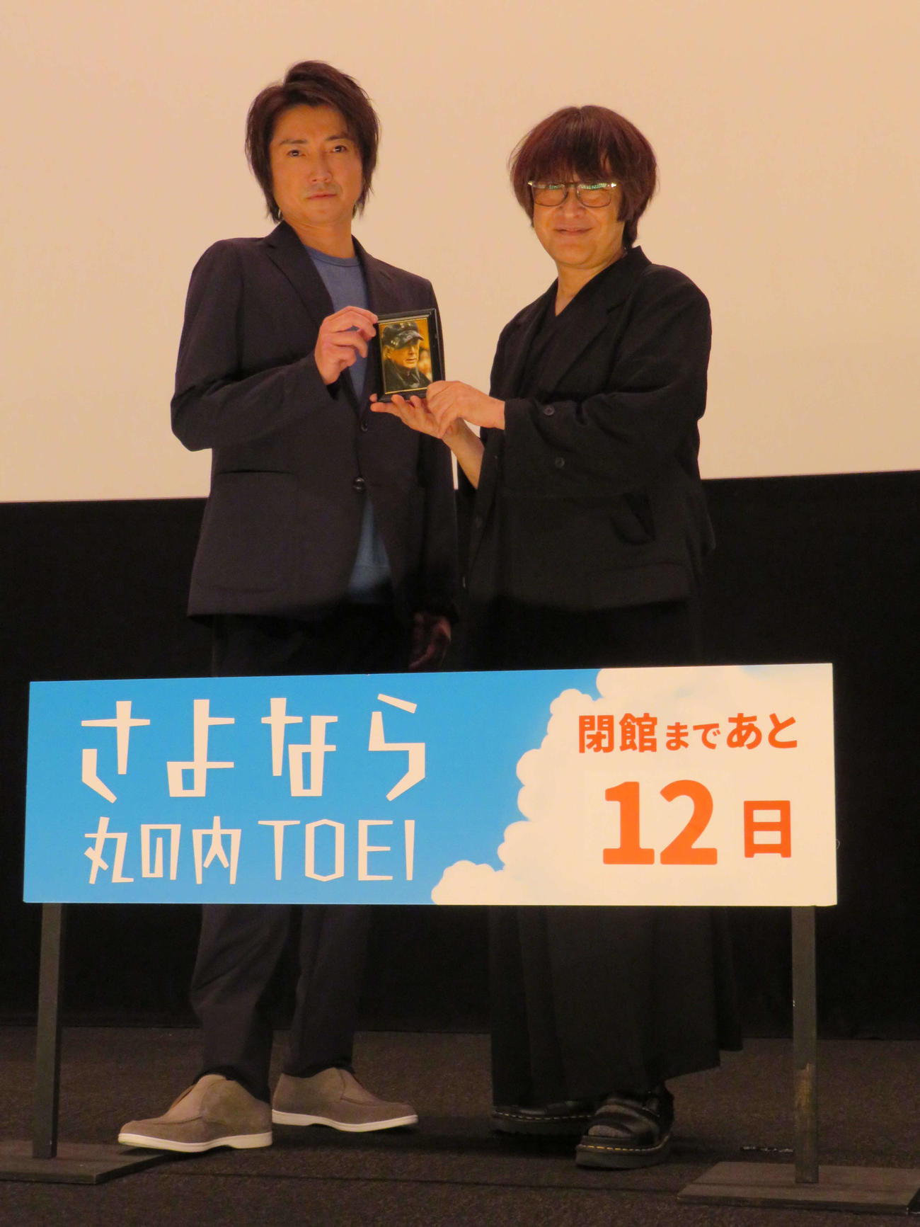 「さよなら丸の内TOEI」の一環として行われた主演映画「バトル・ロワイアル」上映前舞台あいさつに登壇し、深作欣二監督の写真を手にした藤原竜也（左）と、深作監督の息子の健太氏（撮影・村上幸将）