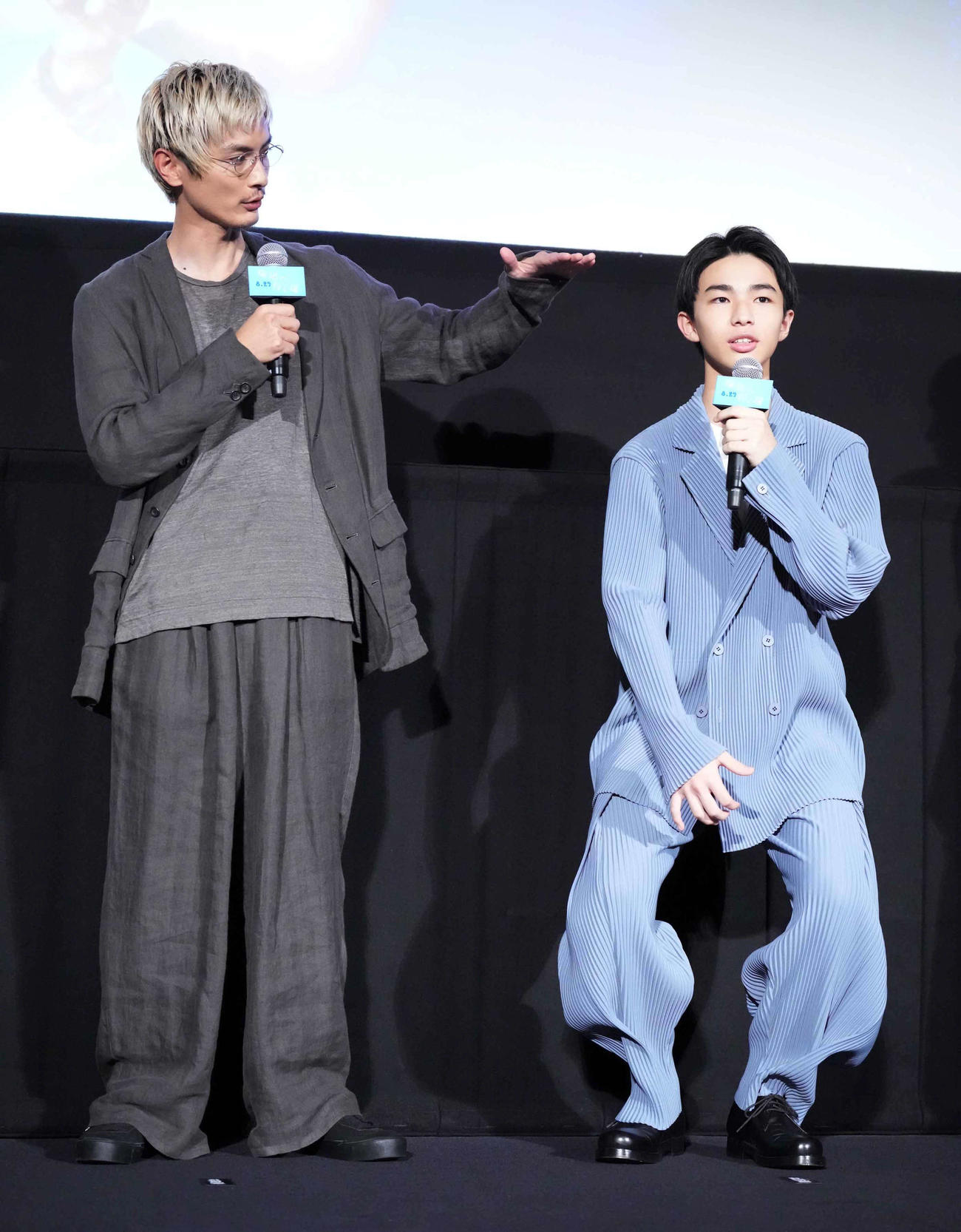 映画「海辺へ行く道」完成披露上映会舞台あいさつで撮影時の身長を再現する原田琥之佑。左は高良健吾（撮影・小沢裕）