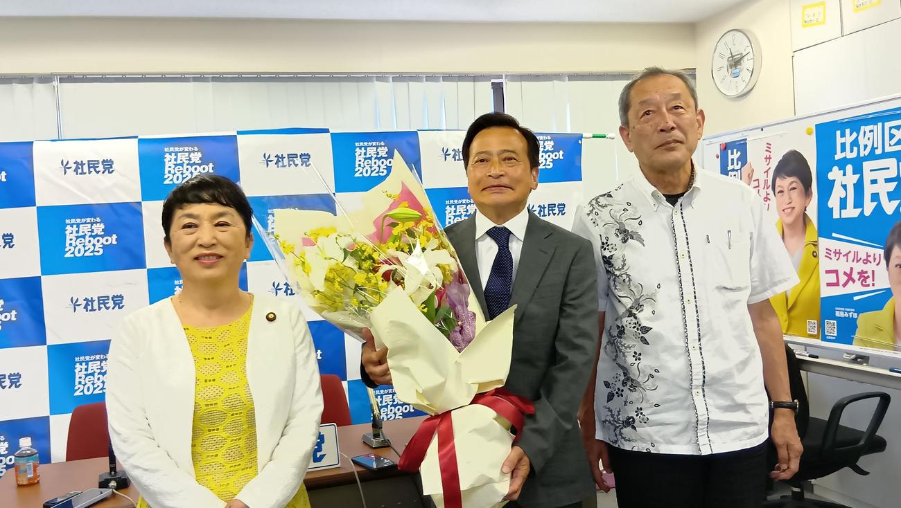 花束を手にするラサール石井氏（中）を祝福する社民党の福島瑞穂党首（左）と服部良一幹事長