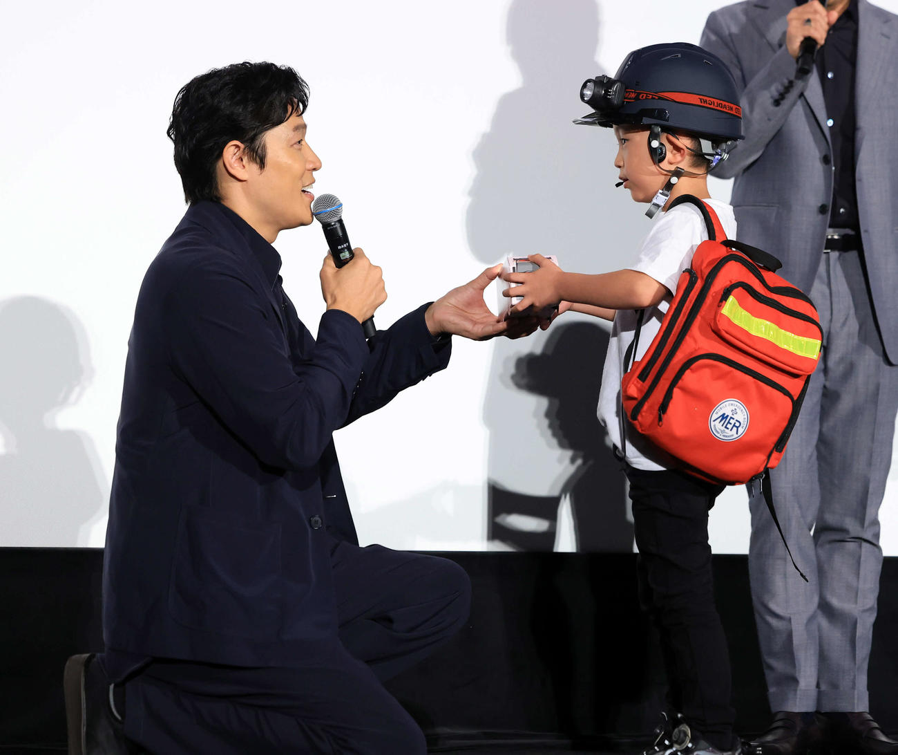 劇場版「TOKYOMER」大ヒット御礼舞台あいさつで、MERの完全装備で訪れたファンの少年に記念品を渡す鈴木亮平（撮影・浅見桂子）