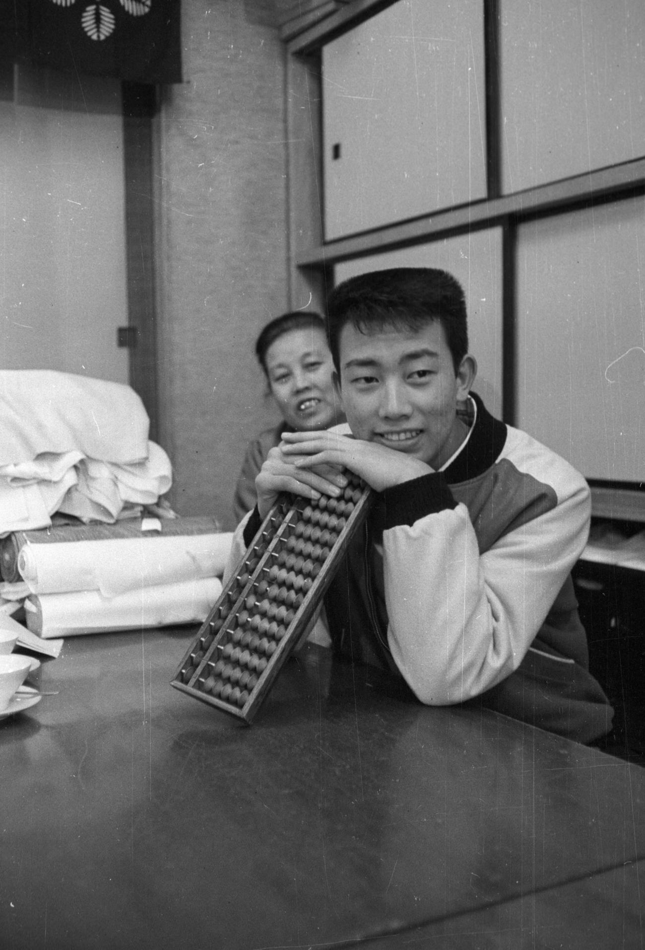 すい星のごとく現れた新人歌手、橋幸夫（1943年5月3日生まれ、9人兄妹の6番目、デビュー曲「潮来笠」で60年レコード大賞新人賞）の人気はうなぎ上り、実家の呉服店もファンの対応に大わらわ。後ろは母親のサクさん（1901年生まれ、89年この母の介護を描いた「お母さんは宇宙人」がベストセラーに）（1961年1月28日撮影）