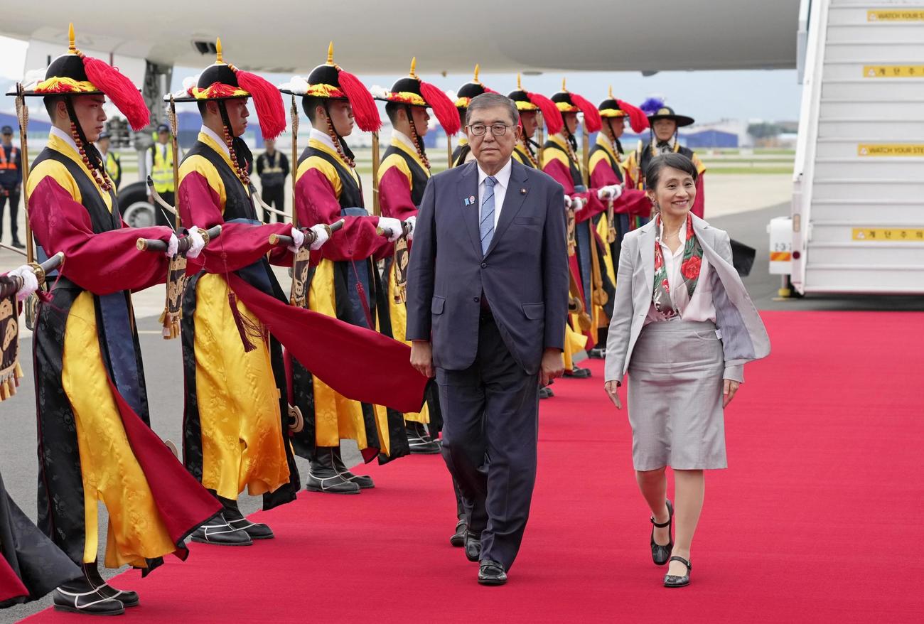 韓国・釜山の金海国際空港に到着し、出迎えを受ける石破首相。右は妻の佳子さん（共同）