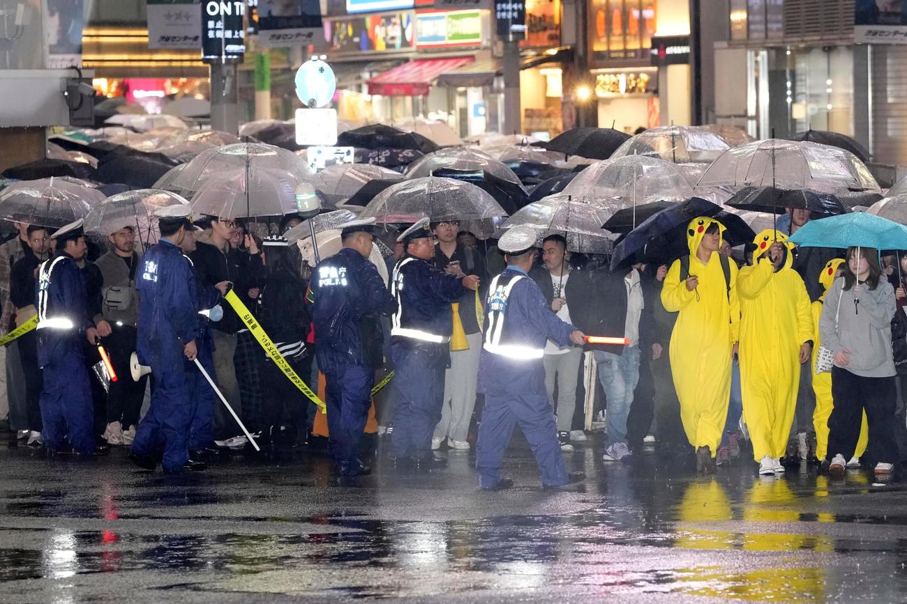 ハロウィーン当日を迎え、東京・渋谷のスクランブル交差点で歩行者を誘導する警察官＝31日夜(共同)