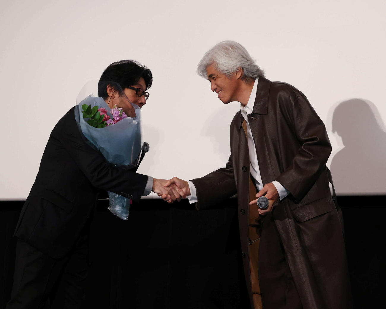 大ヒット御礼舞台あいさつで、紫緩褒賞を受賞し佐藤浩市（右）と握手を交わす阪本順治監督（撮影・増田悦実）