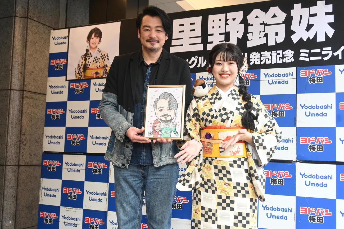 高校の後輩で演歌歌手の里野鈴妹（右）が描いた似顔絵を手に笑顔の小田井涼平（撮影・松浦隆司）