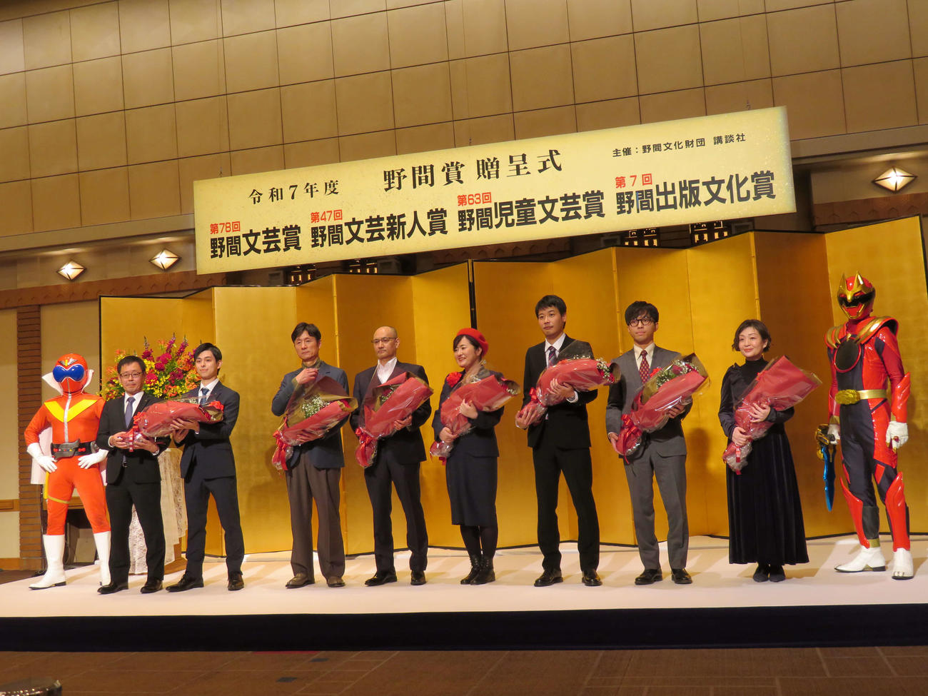 野間文芸賞、野間文芸新人賞、野間児童文芸賞、野間出版文化賞贈呈式に登壇した、左からアカレンジャー、東映の塚田英明氏と松浦大悟氏、李相日監督、吉田修一氏、柚木麻子氏、ピンク地底人3号氏、鳥山まこと氏、村田沙耶香氏、ゴジュウウルフ（撮影・村上幸将）