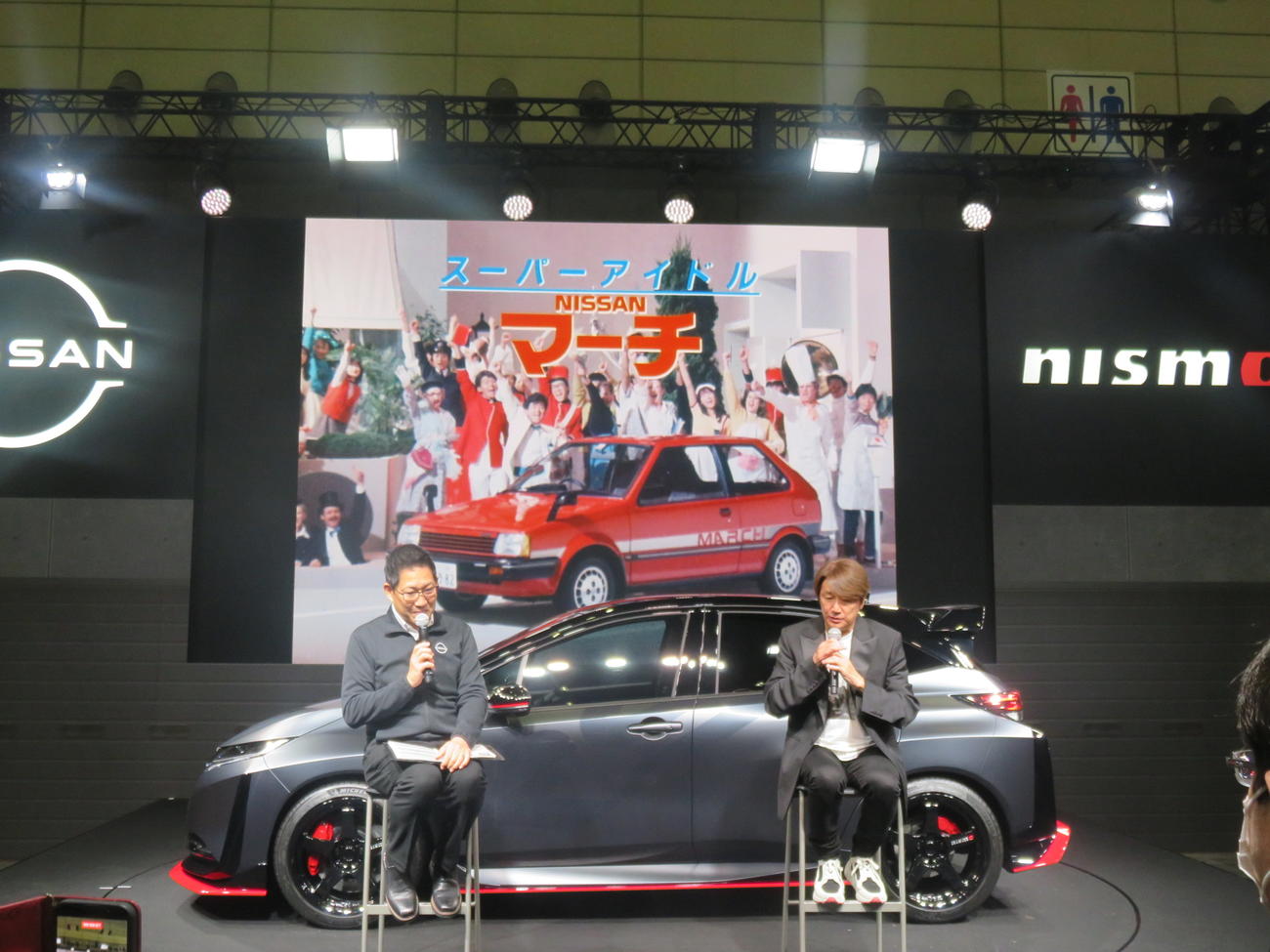 千葉・幕張メッセで開幕した東京オートサロンの日産ブースで「マッチのマーチがあなたの街にリターンマッチ」プロジェクトの発表イベントで、82年の日産マーチのCMを見る近藤真彦（右）