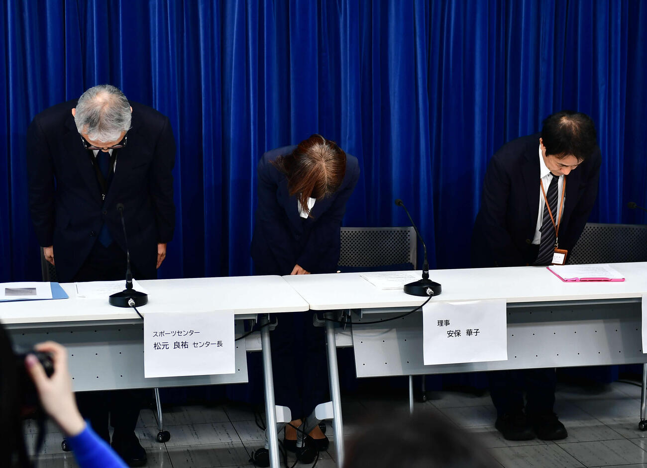 職員の逮捕を受けた会見で頭を下げる、左から松元良祐スポーツセンター長、安保華子理事、小形修一広報局長（撮影・松尾幸之介）