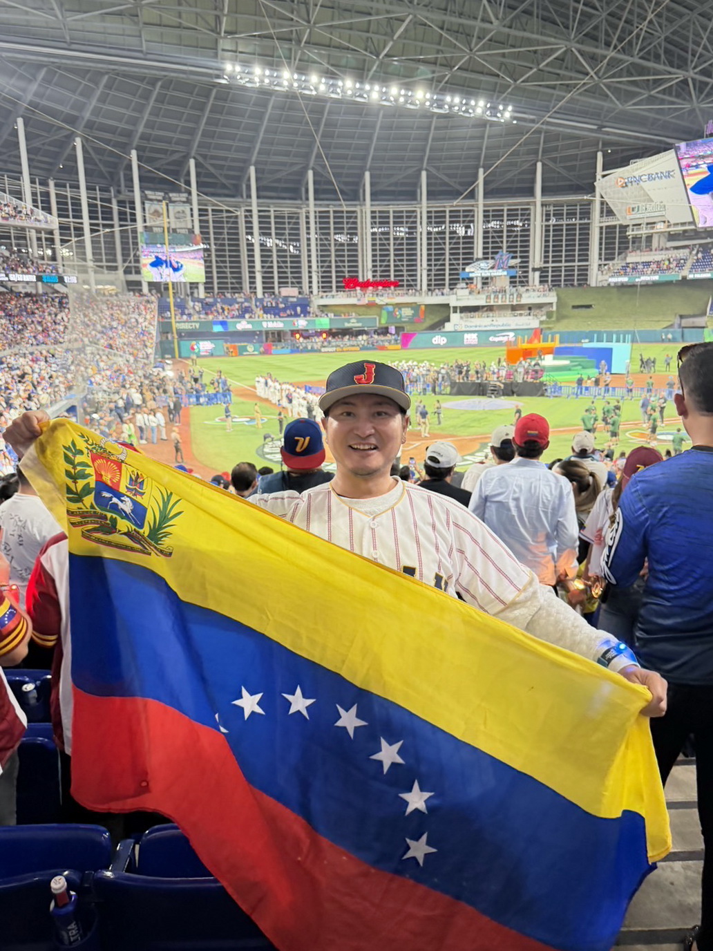 WBC決勝が行われた米ローンデポパークで侍ジャパンユニホーム姿でベネズエラ国旗を掲げるミニタニ（本人提供）