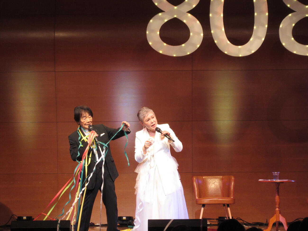 80歳を記念した「80★80」コンサートで紙テープが飛ぶ中で歌う田辺靖雄（左）と九重佑三子（20日、東京・渋谷区けやきホール）
