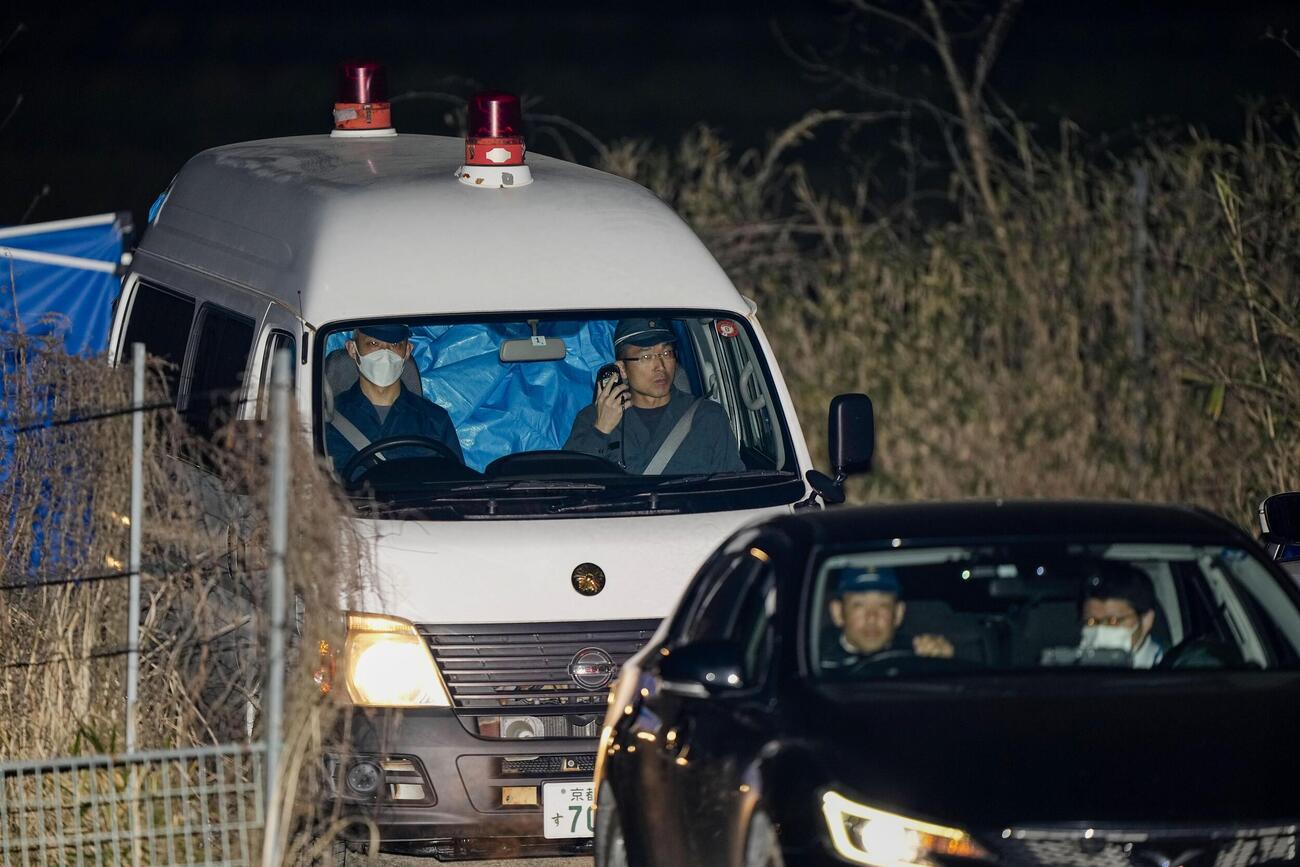 身元不明の遺体が見つかった京都府南丹市の現場付近を出る警察車両。後部座席がブルーシートで覆われていた＝13日午後9時23分(共同)