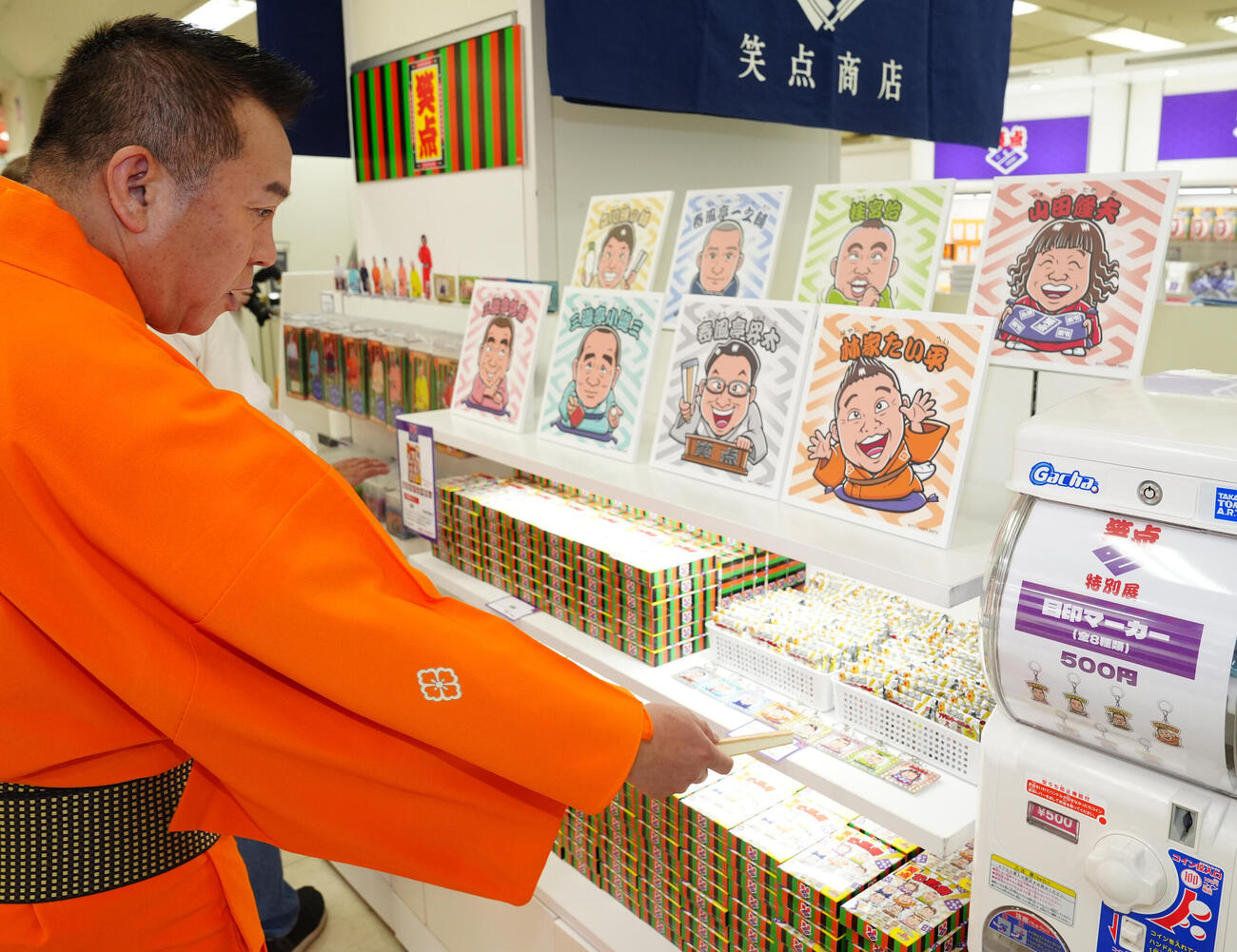 「笑点60周年特別展」で販売されるグッズを指さし、「山田が出てきたらハズレだよ！」と山田隆夫をいじる林家たい平（撮影・江口和貴）