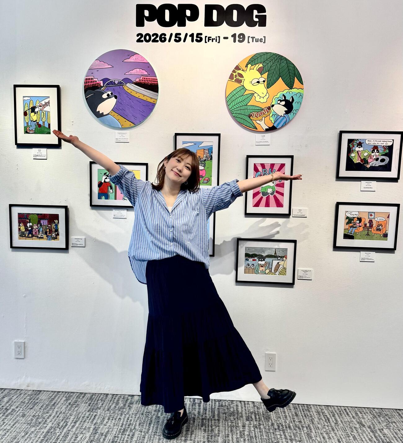 自分の作品をバックにポーズを取る北村まあさ