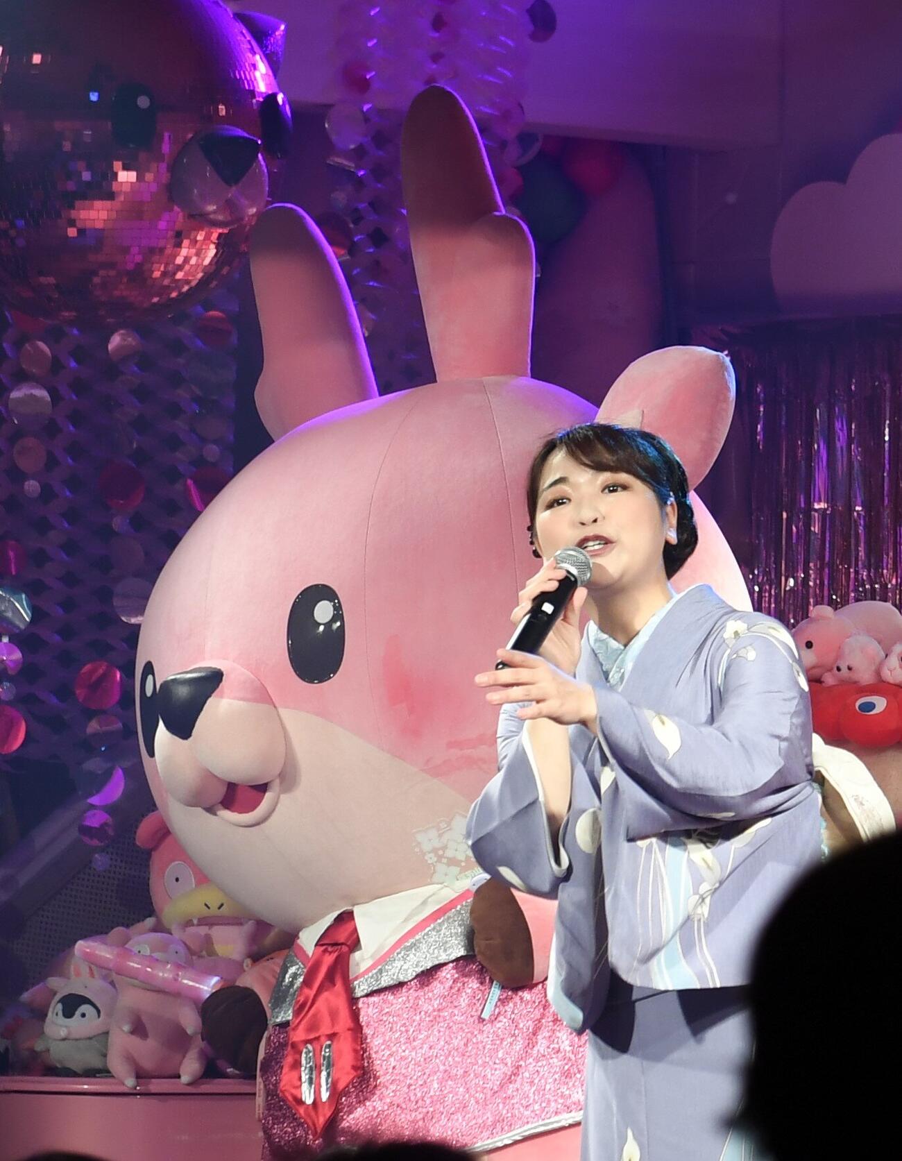 岩下食品の公式キャラクター「イワシカちゃん」をバックに歌う平山花羽