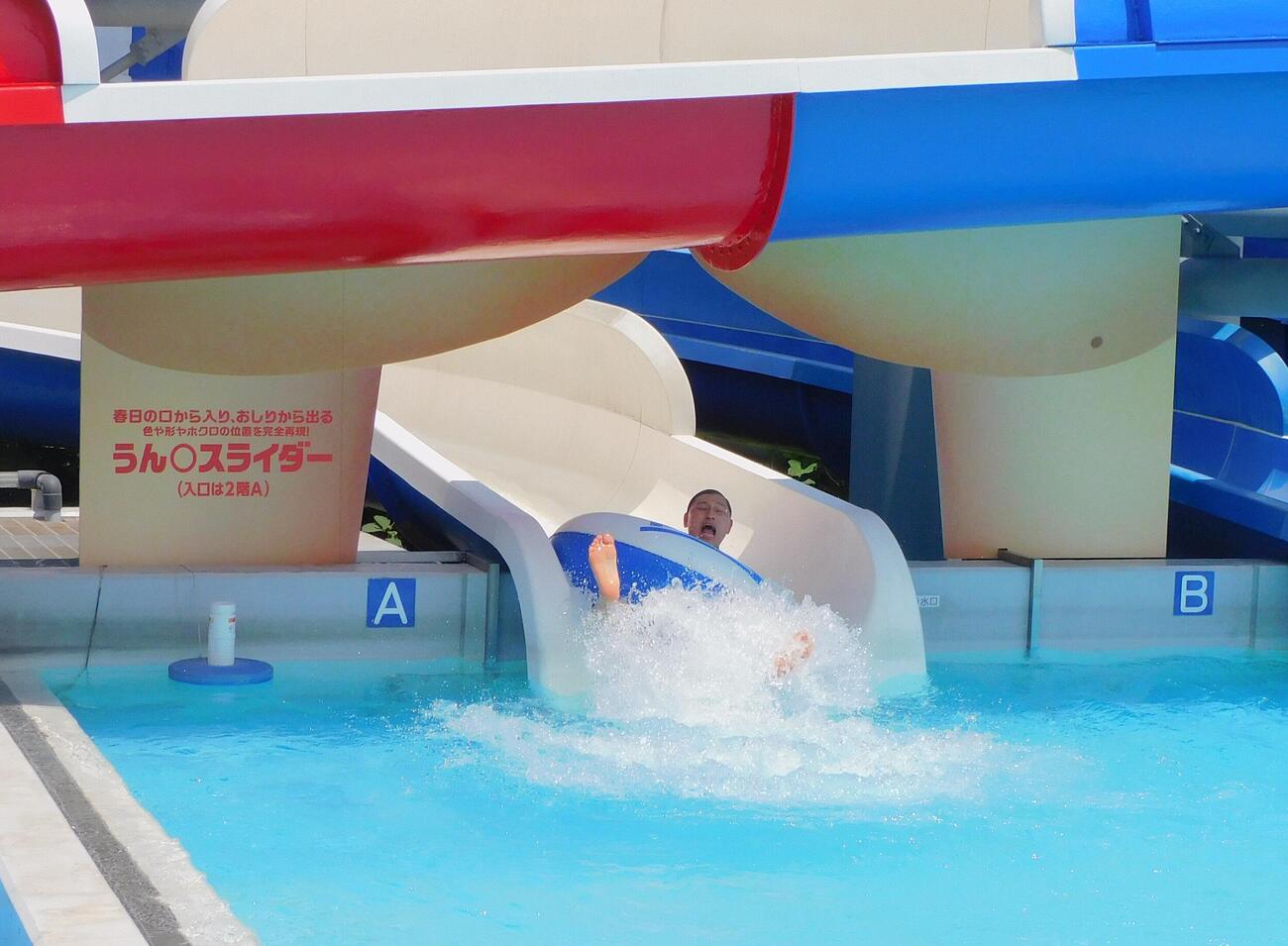 うん○スライダーを体験し、自身のお尻を模した出口から滑り出る春日俊彰
