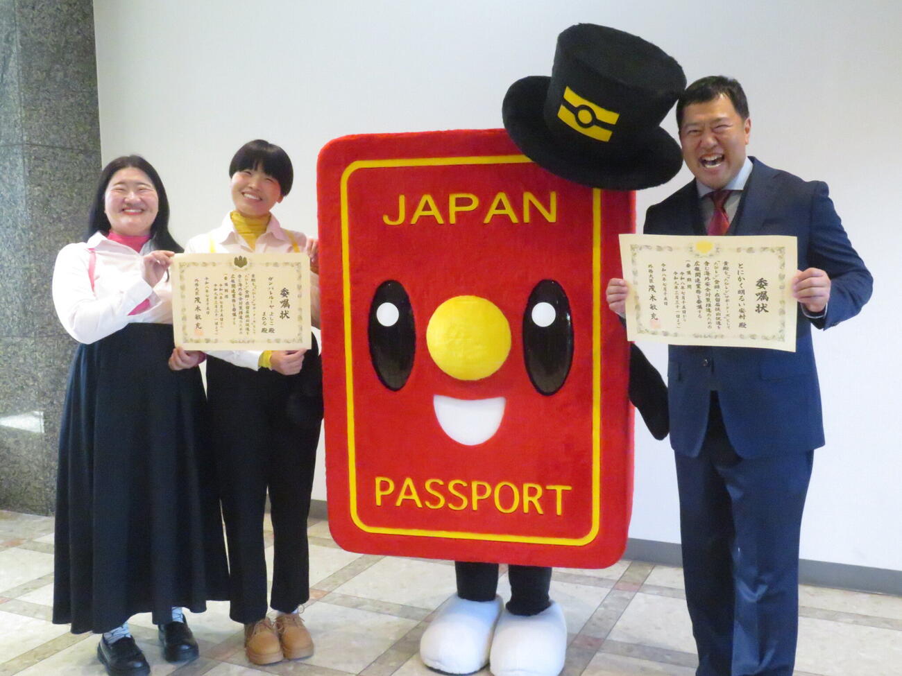 「『たびレジ』サポーターズ」の委嘱状を手に、パスポートのイメージキャラクター「パスポくん」と記念撮影に臨んだ、とにかく明るい安村（右端）、「ガンバレルーヤ」よしこ（左端）、まひる（左から2人目）
