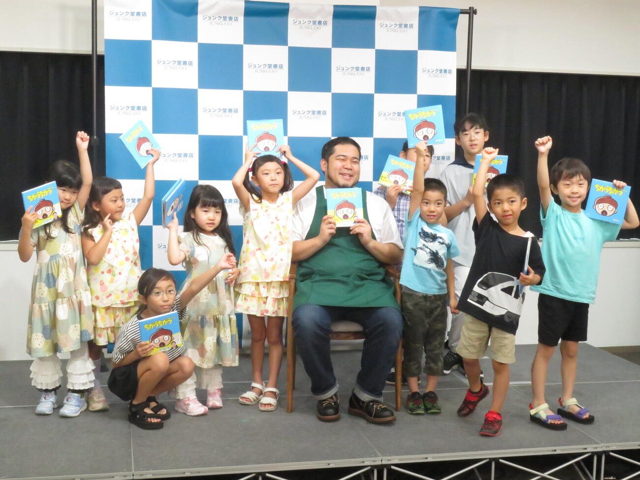 初めて出版した絵本「ちがうちがう」を手に、読み聞かせを行った子どもたちと記念撮影に納まり、笑顔を見せる松井ケムリ（中央）