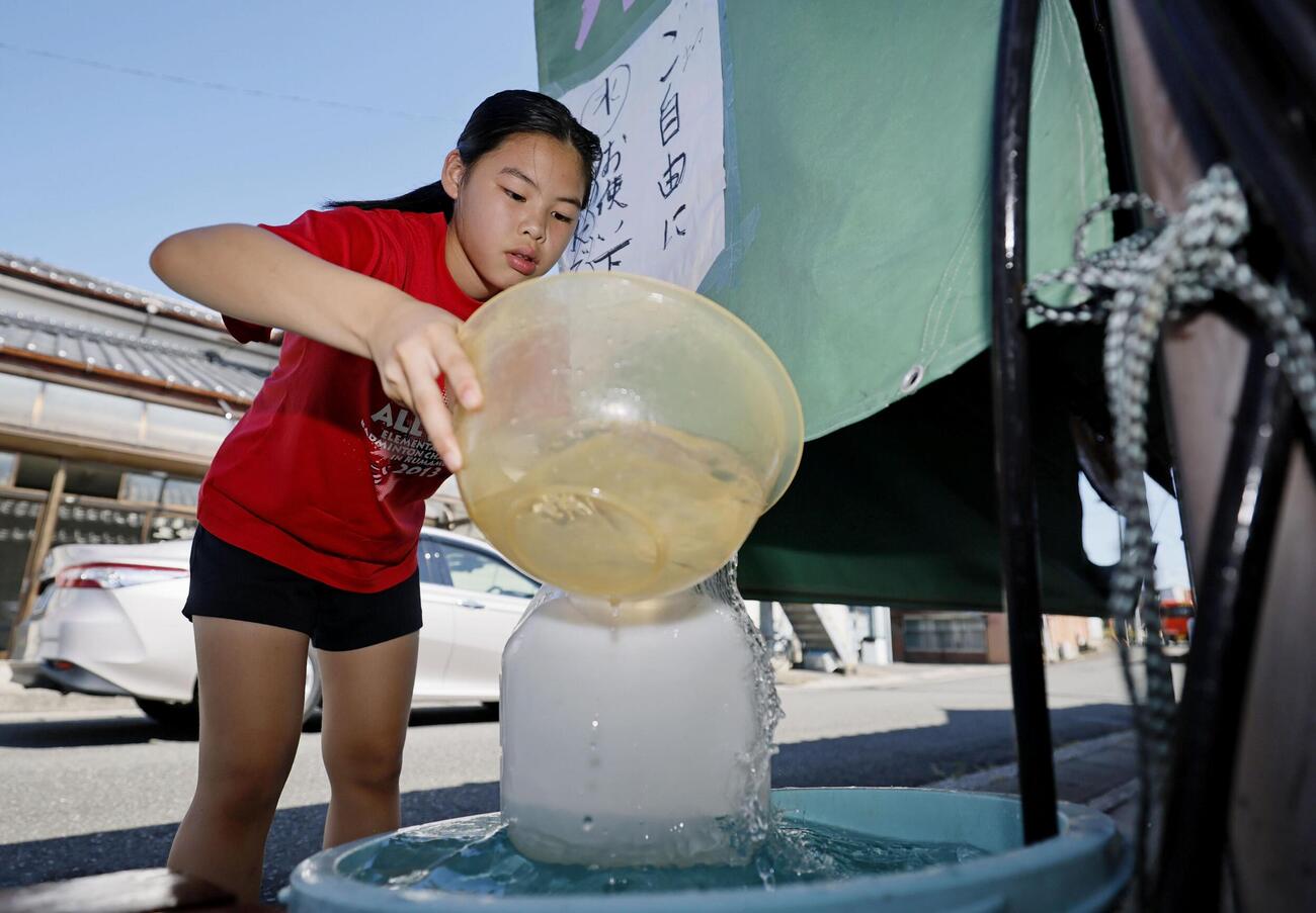 熊本県八代市鏡町の鮮魚店で、地下水を容器に移す女子児童。店を夫と営む高田景子さんは「水は生活に必須。店は営業できないが、地域に少しでも元気を与えられれば」と、無料で提供することを決めた。多くの人が訪れ、持ち帰っていた＝1日午前9時38分（共同）