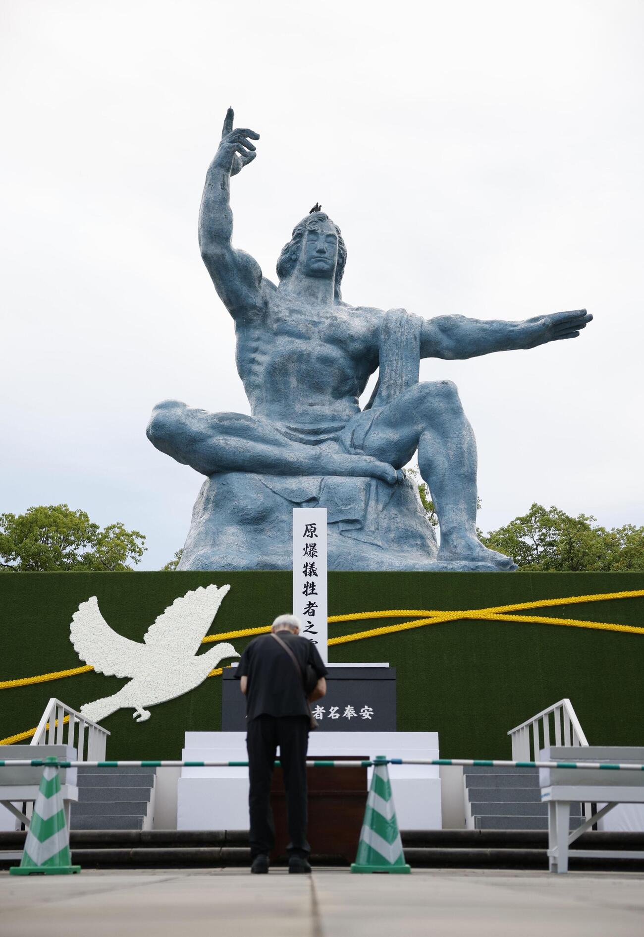 被爆から81年の原爆の日を迎え、長崎市の平和祈念像の前で手を合わせる人（共同）