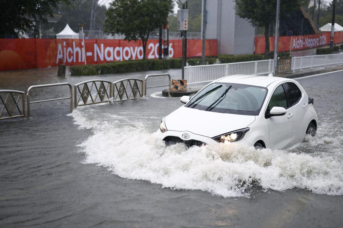 大雨で水があふれた道路を走る車。奥は愛知・名古屋アジア大会の横断幕（共同）