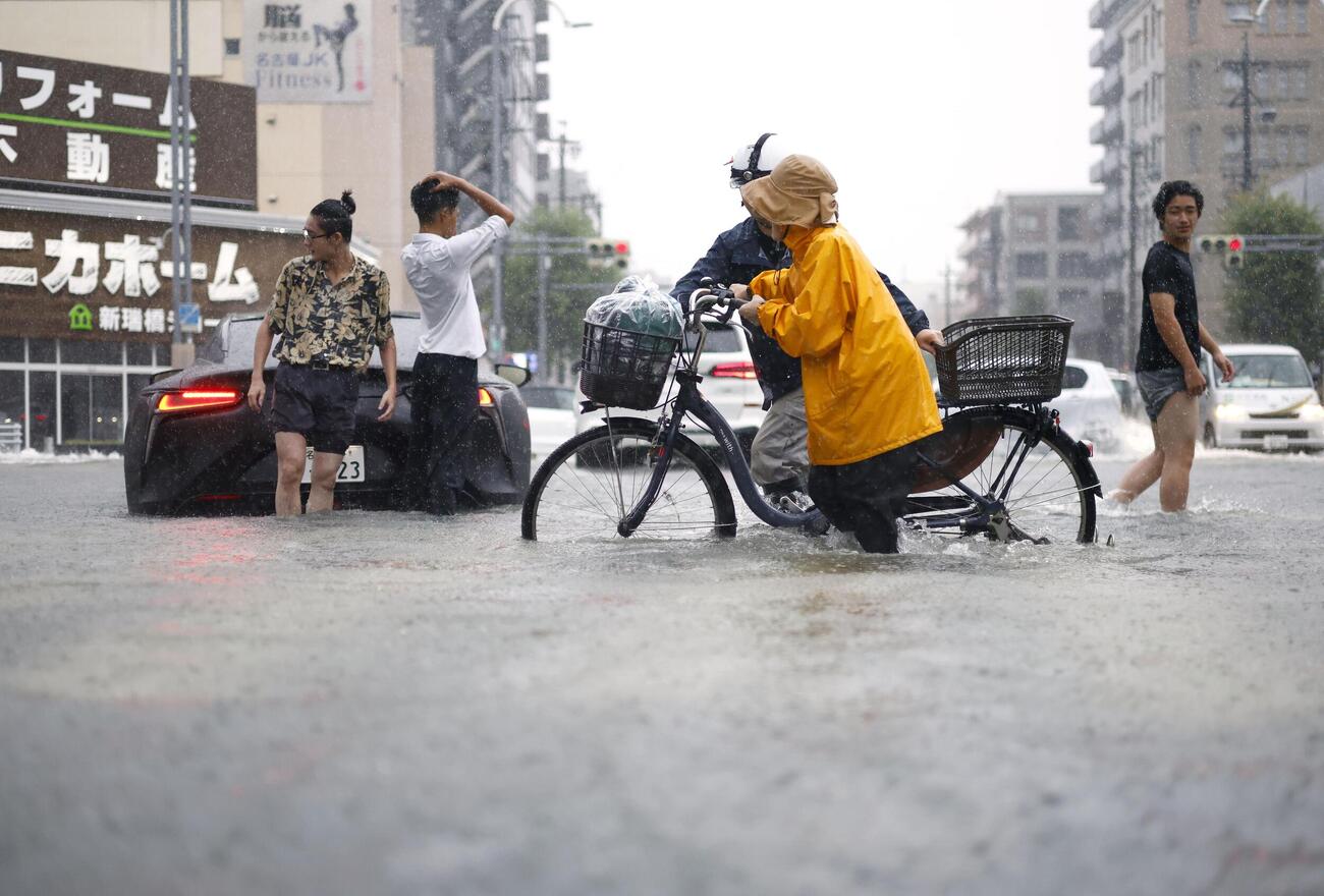 大雨で水があふれた道路を行き交う人たち。車が立ち往生していた（共同）
