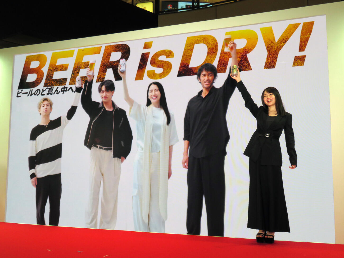 他のCM出演者が映し出されたビジョンの前で乾杯のポーズをとる山田杏奈（右）。ビジョンに映るのは左からTaka、横浜流星、長澤まさみ、阿部寛