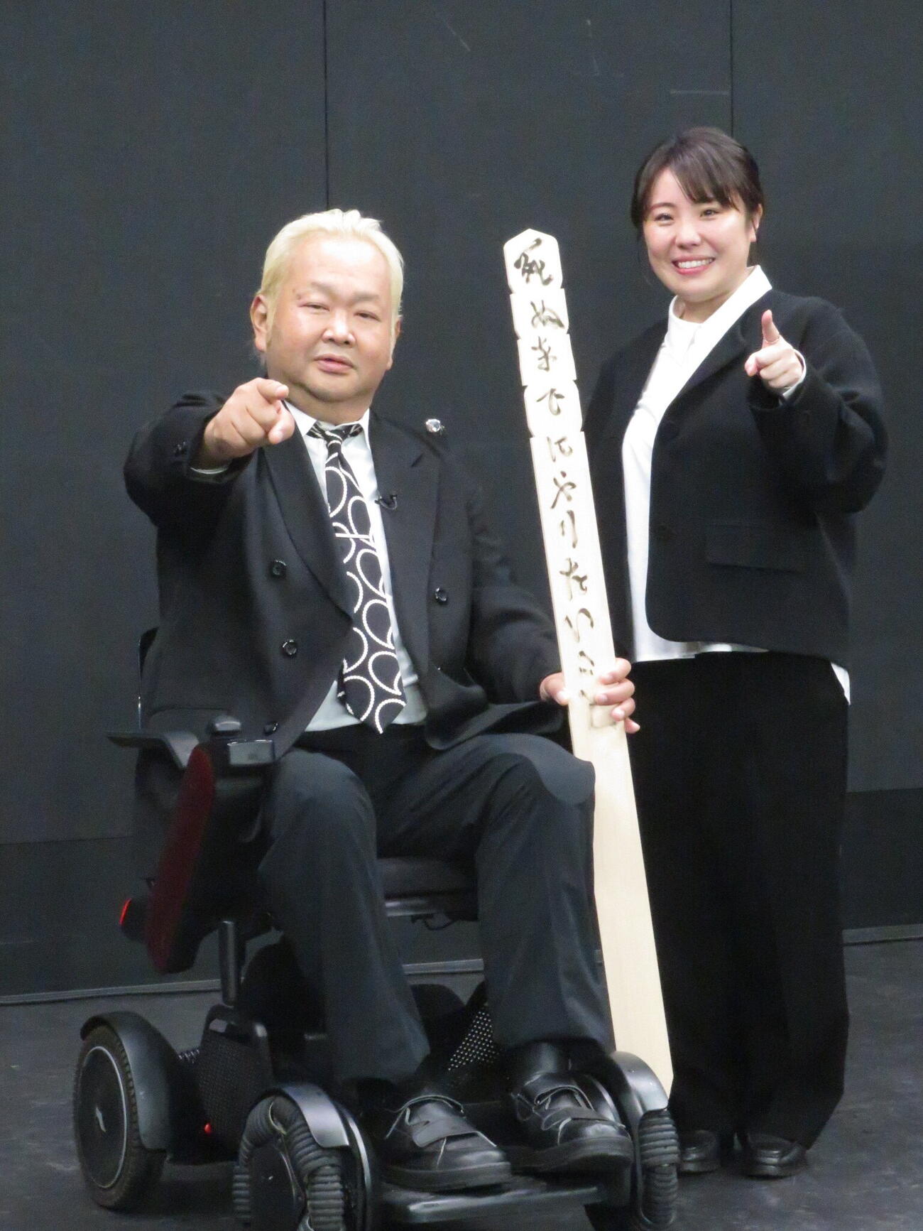 卒塔婆に「死ぬまでにやりたいこと」と番組名を書き、かつて対戦した大仁田厚の「ファイヤー」のポーズをつくるハチミツ二郎（左）と吉本興業の山岸未歩さん