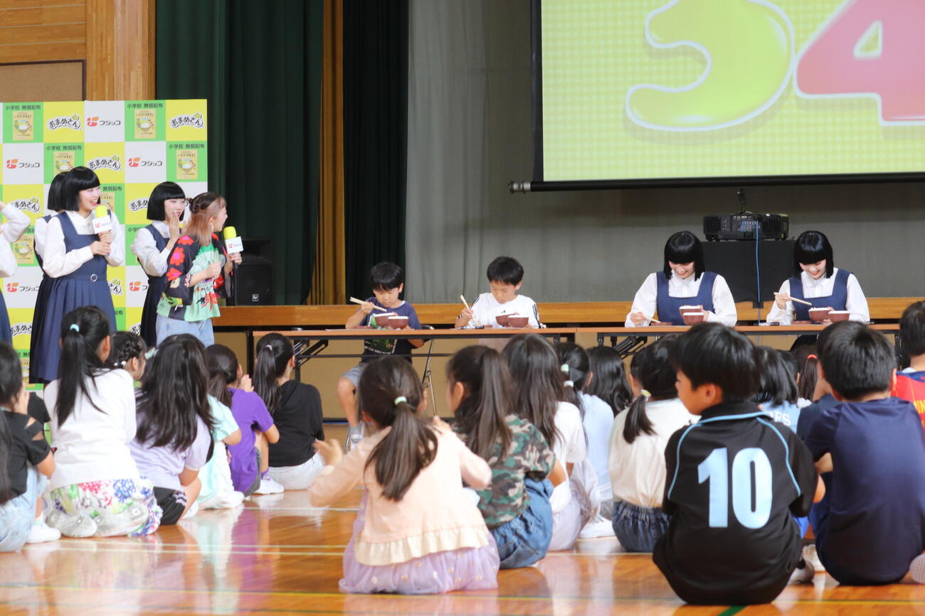 フジッコ豆の日イベント「いただきます読本」公開授業で豆つかみゲームに挑戦した荒川区立尾久第六小学校の児童とアバンギャルディ

