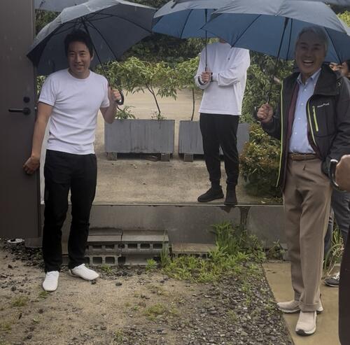 独自システムで浄化される恵みの雨の中、説明を受けて笑顔を見せる石原伸晃氏(右)