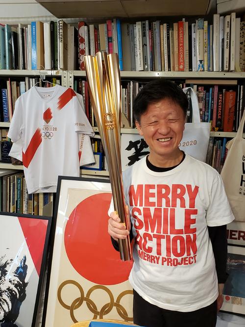 聖火ランナーに選ばれ、「トーチキス」セレモニーで使ったトーチを手に笑顔をみせるアートディレクター水谷孝次氏
