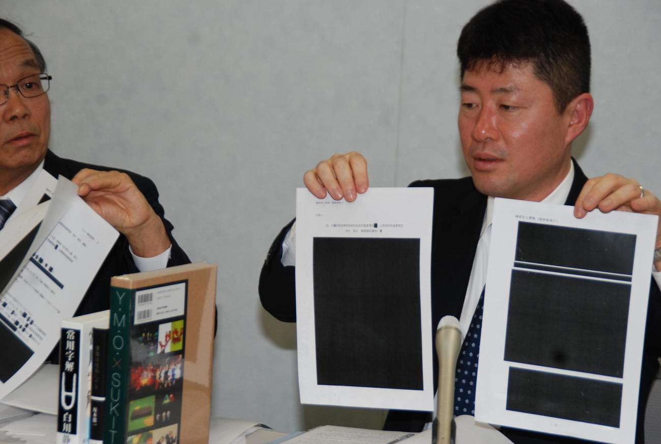 真っ黒に塗りつぶされた情報公開資料を手に記者会見をする妻側代理人弁護士（撮影・松浦隆司）