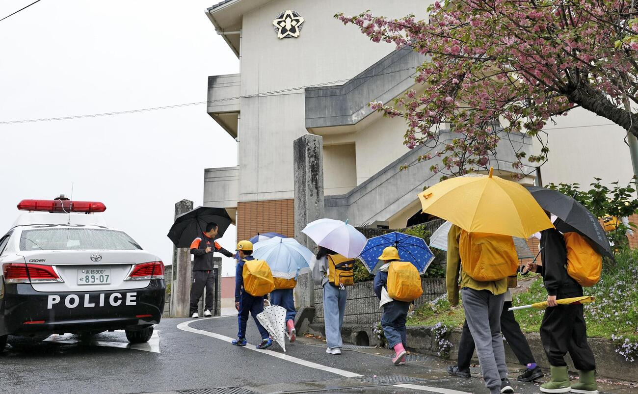 警察官らに見守られながら園部小に登校する児童たち。安達結希さんの行方不明から1カ月となった＝23日午前、京都府南丹市（共同）