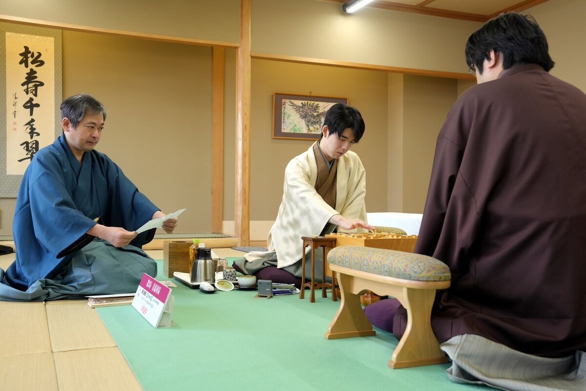 立会人の行方尚史九段（左）が初日に藤井聡太名人（中央）が封じた指し手を読み上げて名人戦第2局は対局を再開。右は挑戦者の糸谷哲郎九段（日本将棋連盟提供）