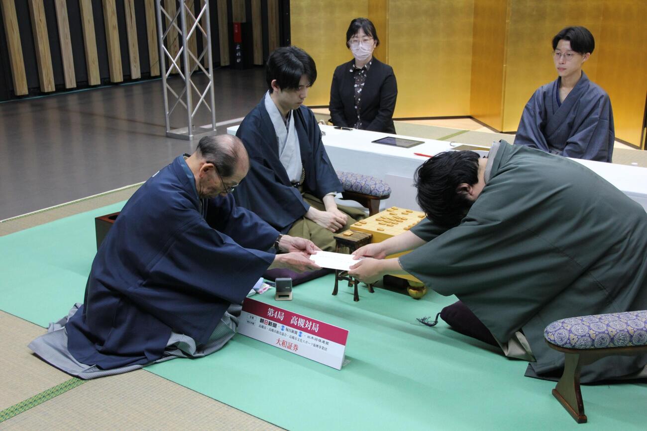 立会人の桐山清澄九段（左）に封じ手の封筒を手渡す糸谷哲郎九段（右）、中央は藤井聡太名人（日本将棋連盟提供）