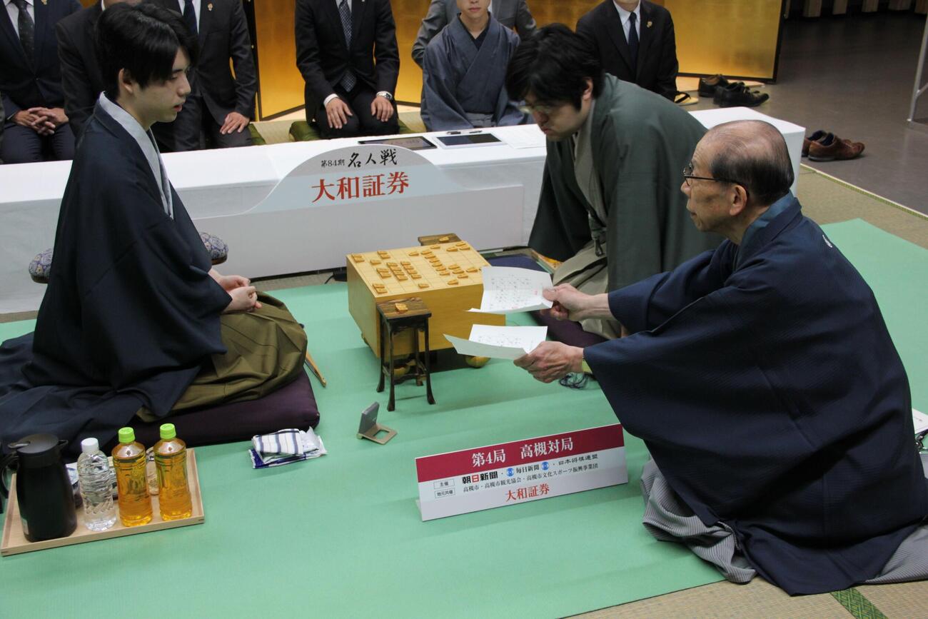 立会人の桐山清澄九段（右）が示した糸谷哲郎九段の封じ手を確認する藤井聡太名人（左）（日本将棋連盟提供）