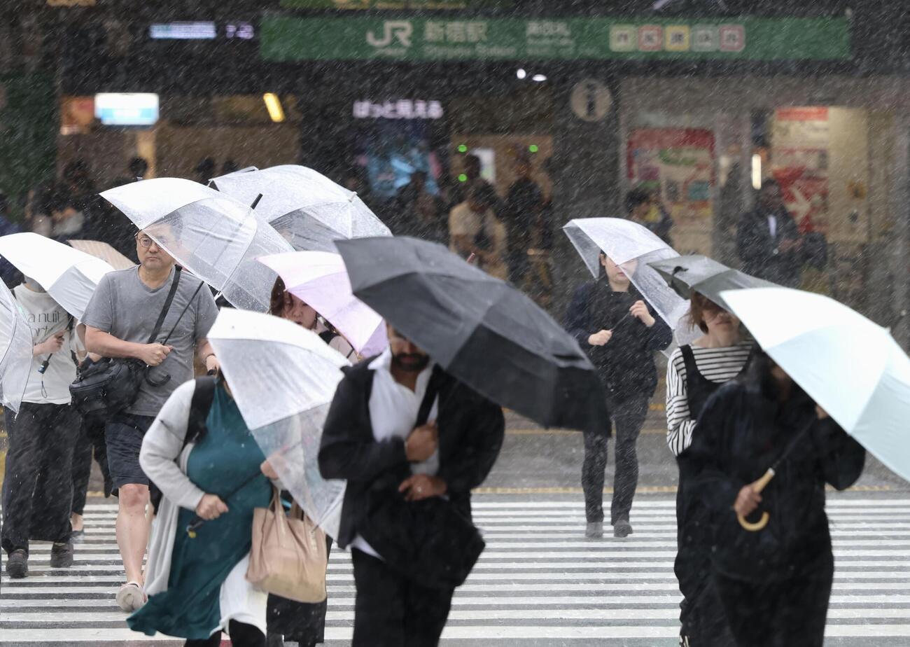 台風6号の影響による強い風雨の中、東京・新宿駅前の横断歩道を渡る人たち＝3日午前7時40分ごろ（共同）