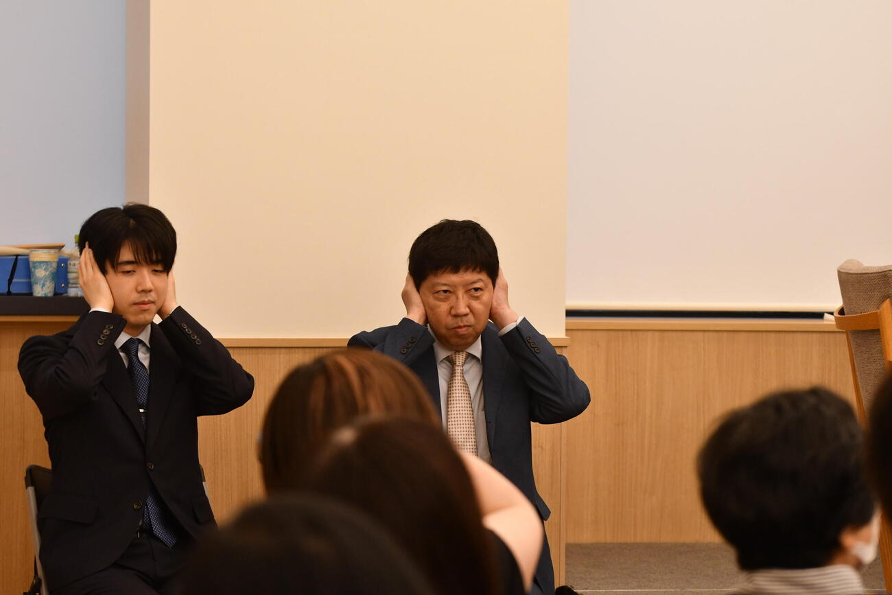 斎藤明日斗六段と伊藤匠2冠の作戦タイム中に耳栓をして耳をふさぐ藤井聡太6冠（左）と師匠の杉本昌隆八段（右）