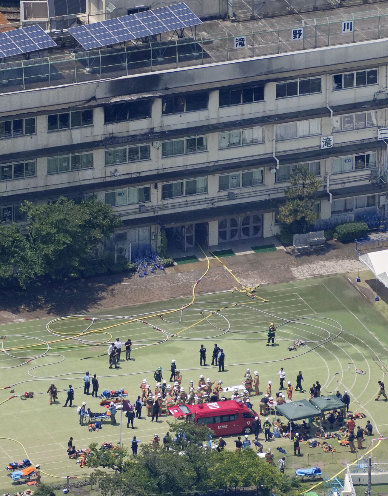 火災があった東京都北区立滝野川第三小の校庭に集まる消防隊員ら＝19日午後0時4分（共同通信社ヘリから）(共同)