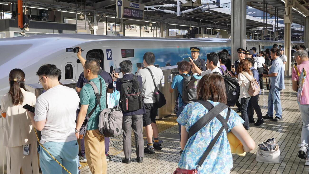 ディズニーキャラクターが側面に描かれた東海道新幹線の特別車両を見る人たち（共同）