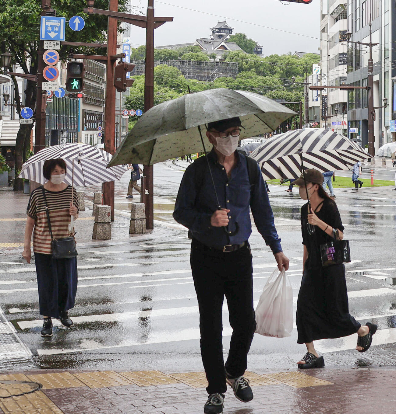 傘を差して熊本市内を歩く人たち＝25日午前（共同）