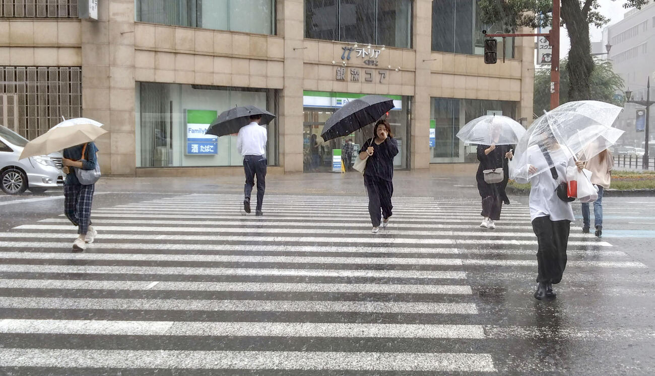 雨の中、傘を差して熊本市内を歩く人たち＝25日午前（共同）